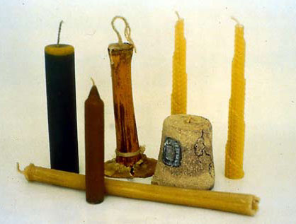A display of homemade candles from West Africa (from left to right): stained candle moulded in PVC pipe, coloured wax with trimmed tip,  candle still inside of bamboo mould, 2 candles rolled from wax foundation sheets, decorated candle from plastic cup mould, candle from bamboo mould (bottom).